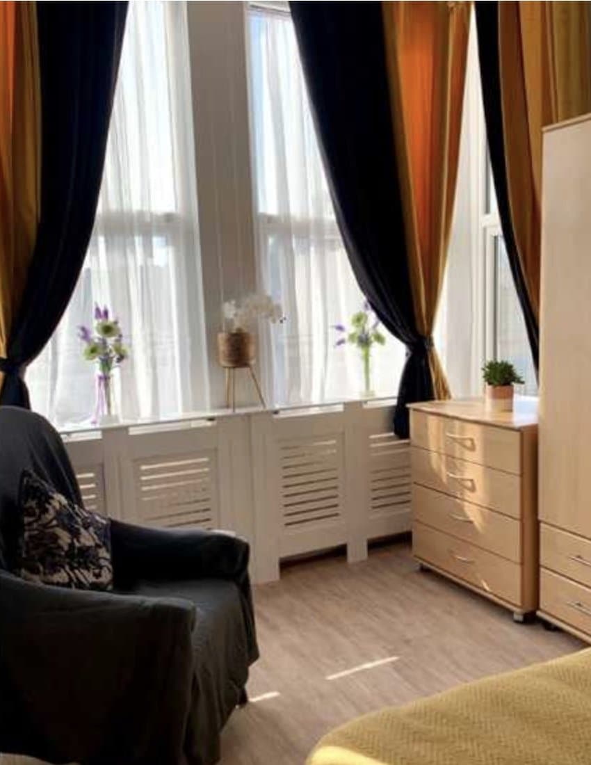 A bright bedroom with a wardrobe, armchair and tall windows