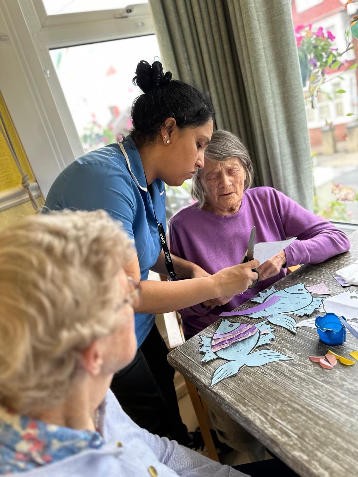 A carer helping two residents with a paper craft activity